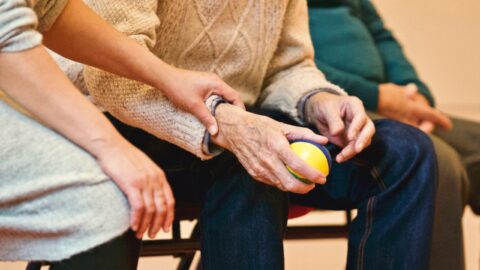 an elderly person holding a stress ball while a loved on holds gently holds their arm