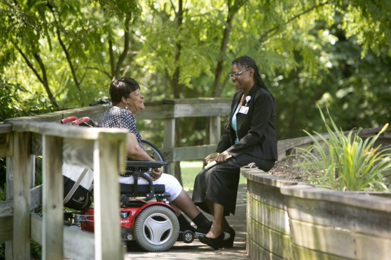 a social worker talking with an elderly patient in a wheelchair in a park