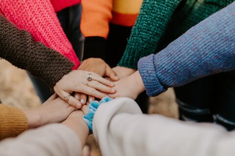women wearing sweaters putting their hands together in the center for a circle