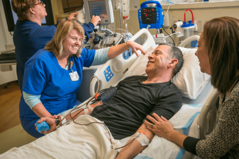 research coordinator in medical scrubs talking with a patient in a hospital bed