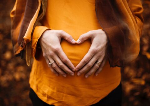 pregnant woman with her hands over her stomach in the shape of a heart