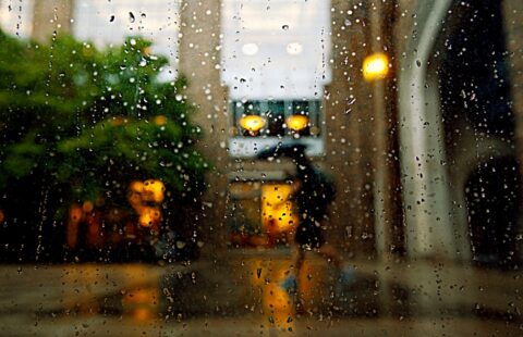 person walking in the rain as viewed through a window