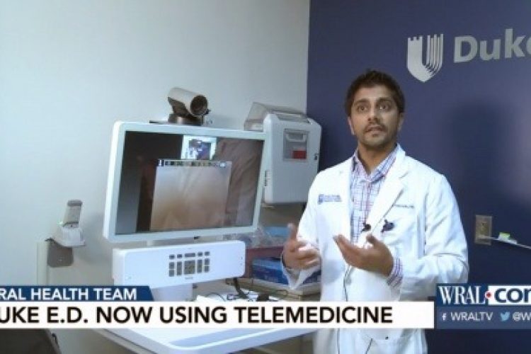 Neel Kapadia, MD standing in front of a computer with a camera which is used for telehealth visits