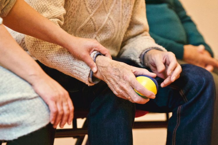 an elderly person holding a stress ball while a loved on holds gently holds their arm