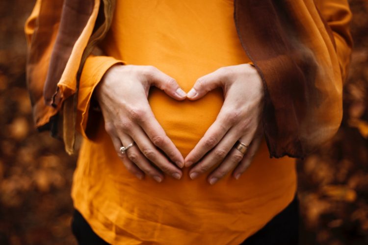 pregnant woman with her hands over her stomach in the shape of a heart